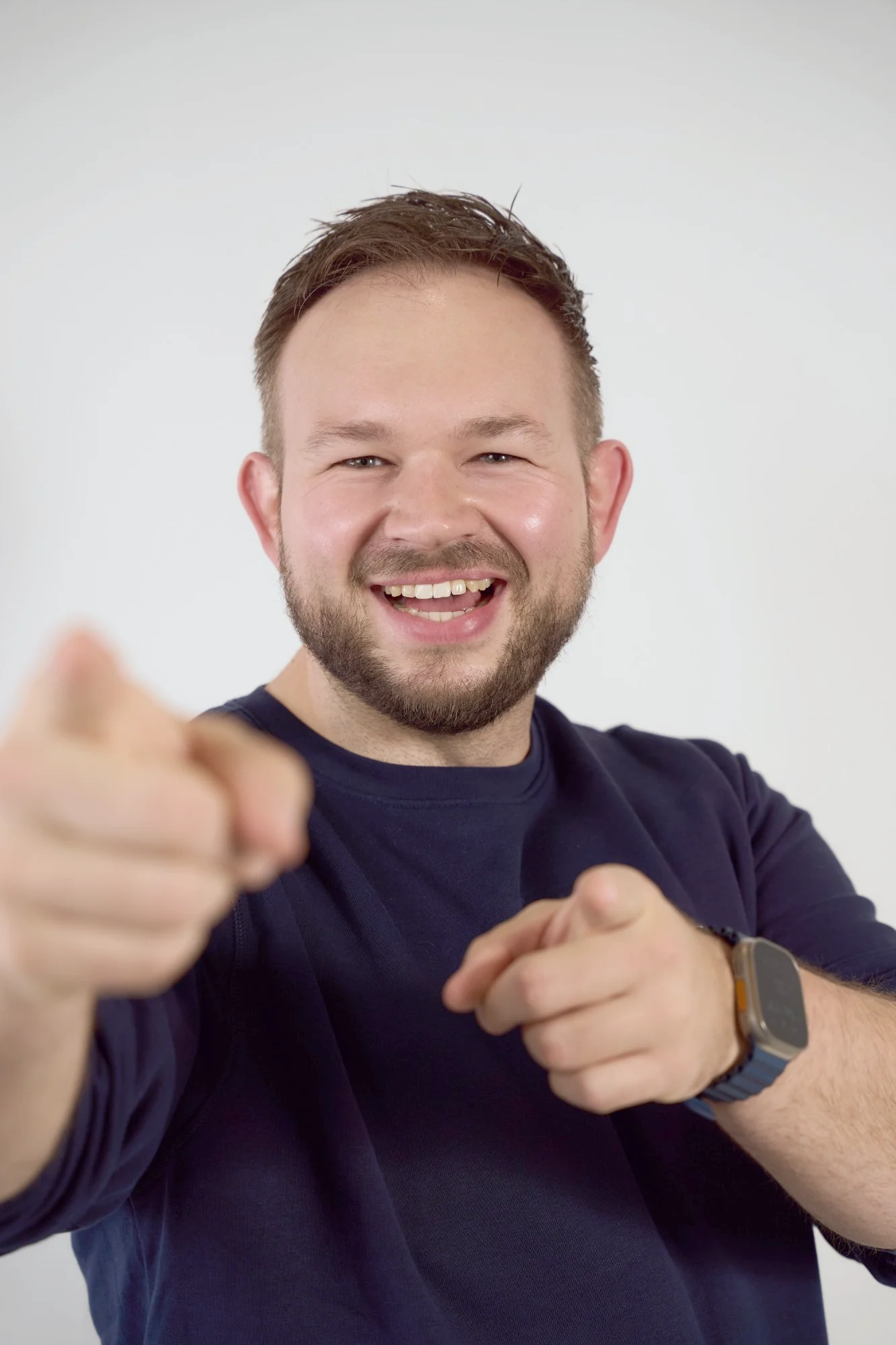Daniel Rohregger laughing at the camera and pointing at you with both hands, in front of a light studio backdrop