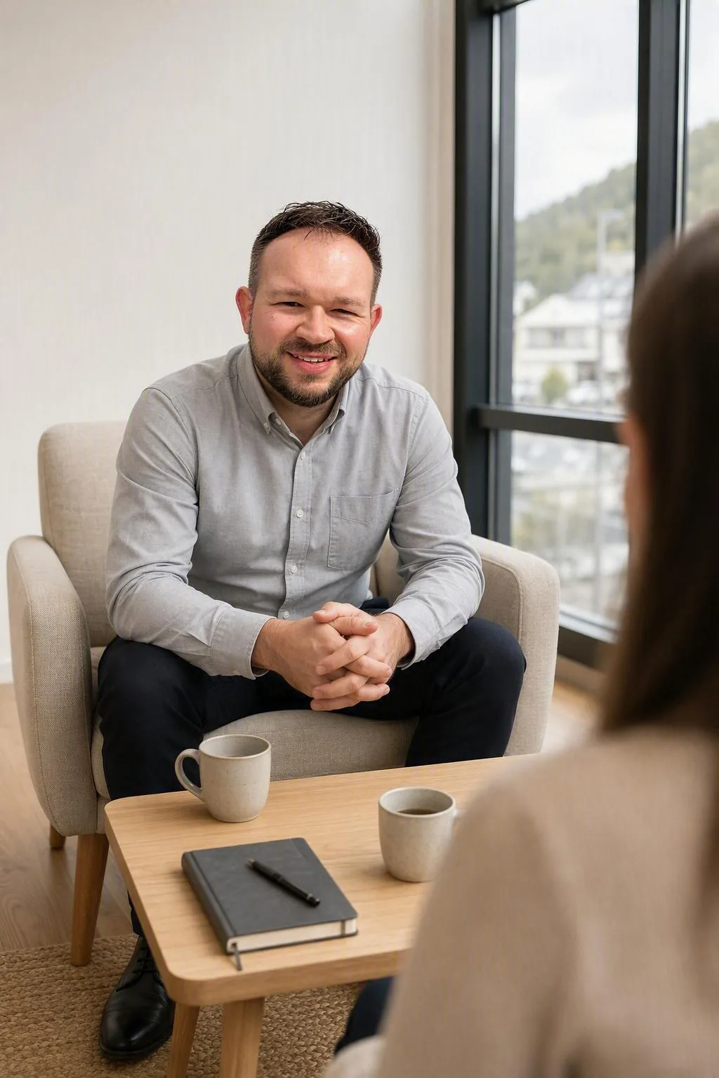 AI-generated scene: a person sits in an armchair in conversation with a second person, with a low table between them holding a notebook and two cups