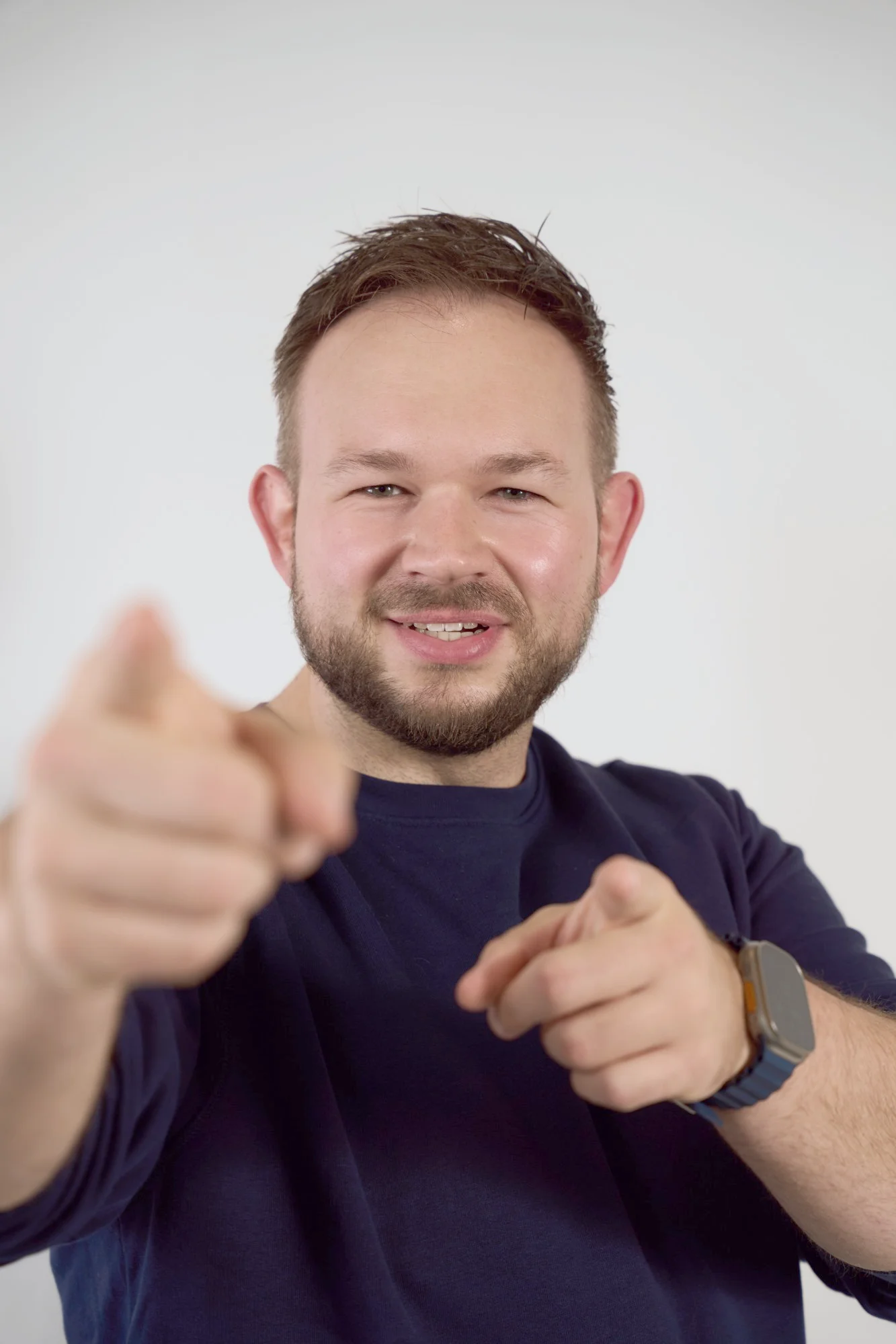 Daniel Rohregger smiling at the camera and pointing at you with both hands, in front of a light studio backdrop